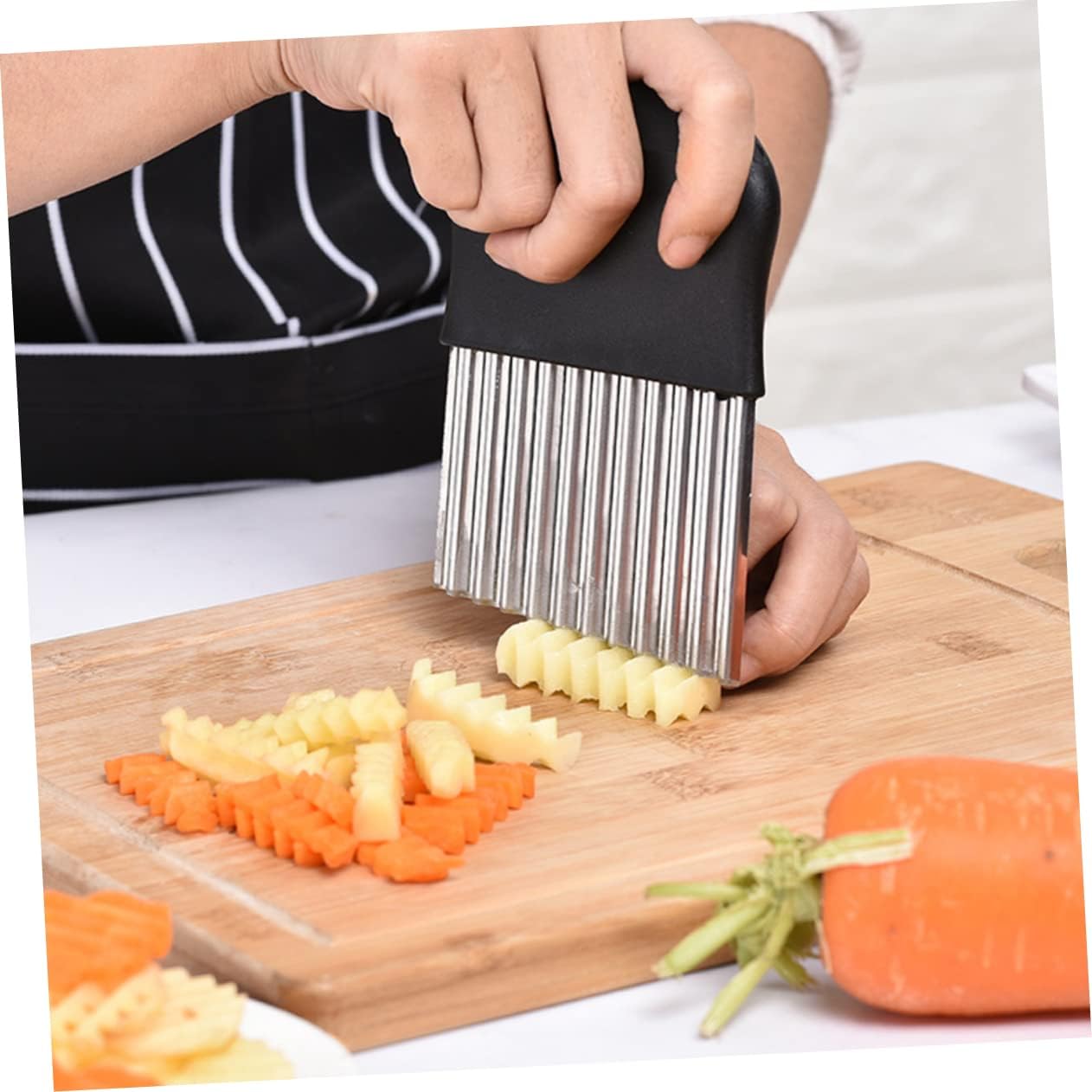 Person using a vegetable slicer to cut carrots and potatoes on a wooden cutting board.